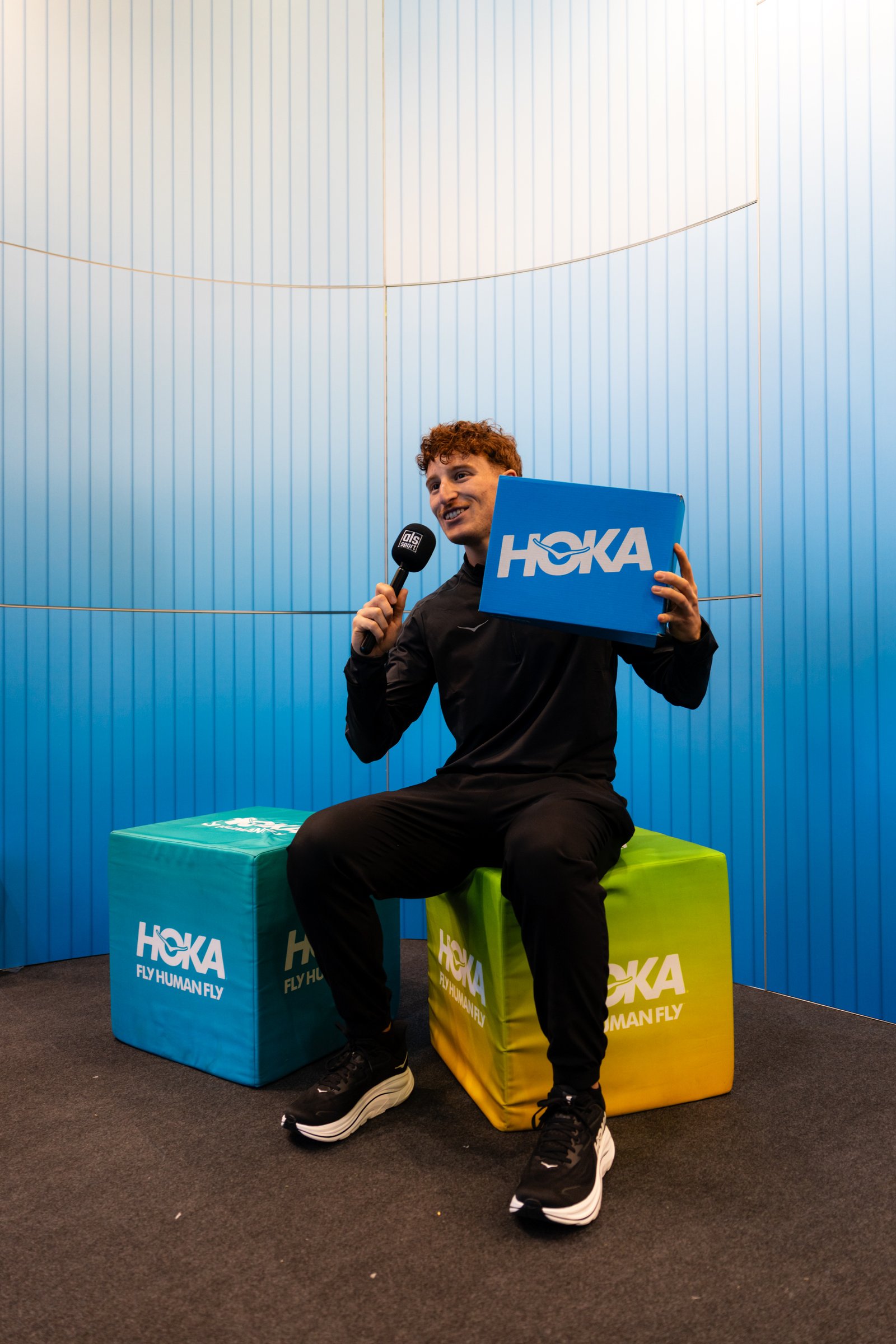 Guille con micrófono y una caja de HOKA en la feria del Medio Maratón de Sevilla